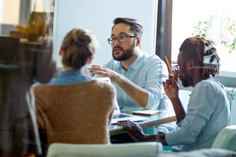 Students in a Lean Six Sigma class sit at a table discussing solutions to a problem.