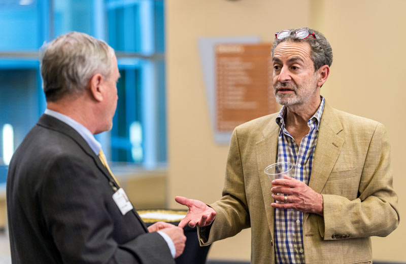 Two faculty members talk about curriculum at a reception.