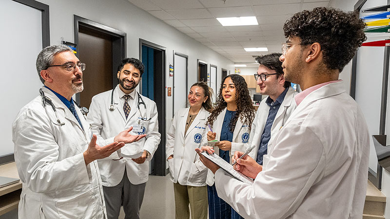 Medical students in white coats compare notes with an advisor in the NEOMED Free Clinic.