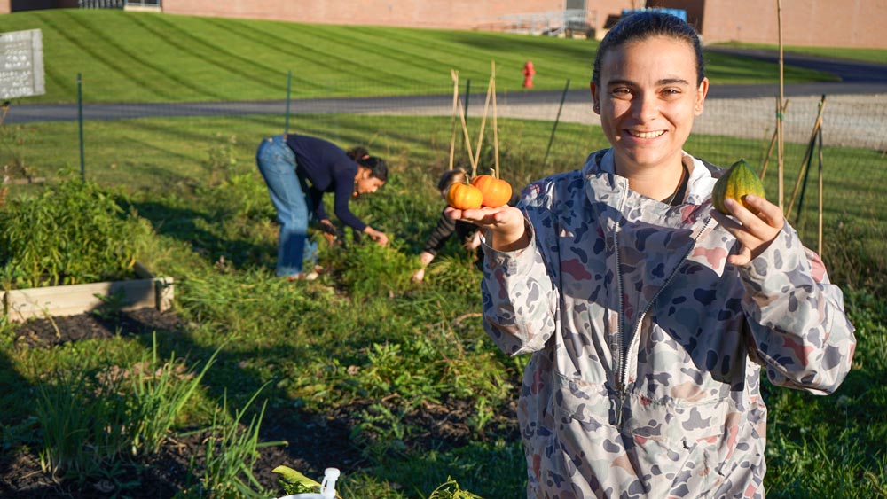 A student holds miniature pumpkins in the garden.