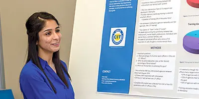 A person stands beside a research poster and explains its charts and written findings.