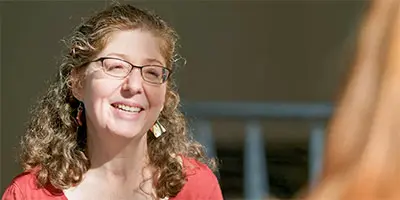 A person wearing glasses speaks with someone off-camera in a well-lit indoor setting.