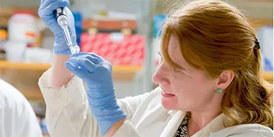 A researcher in gloves and a lab coat uses a pipette while focusing on a sample.