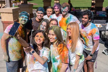 A group of students post for a selfie at a holi celebration on campus.