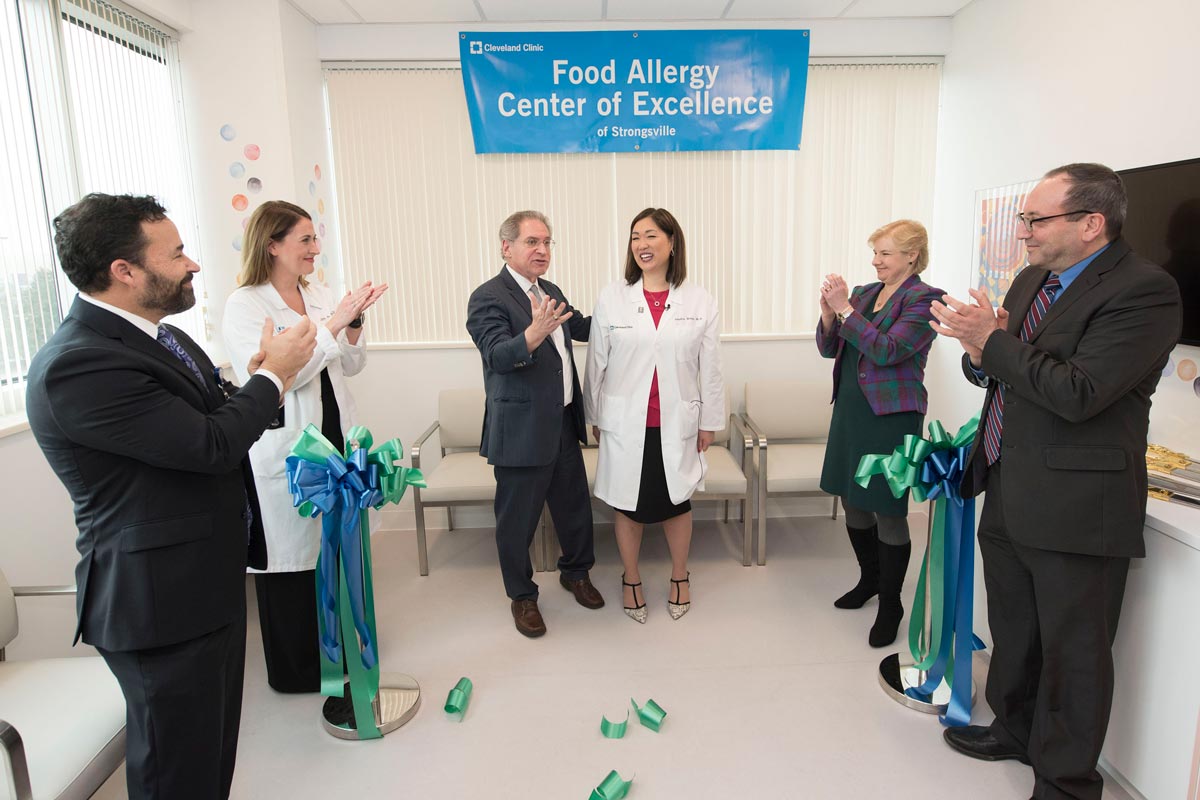 A woman stands with a group of colleagues, who are applauding the ribbon cutting.