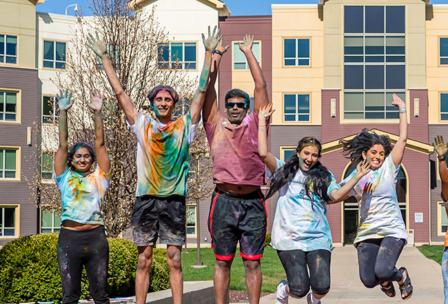 Students jump with arms outstretched during a Holi celebration on campus. 