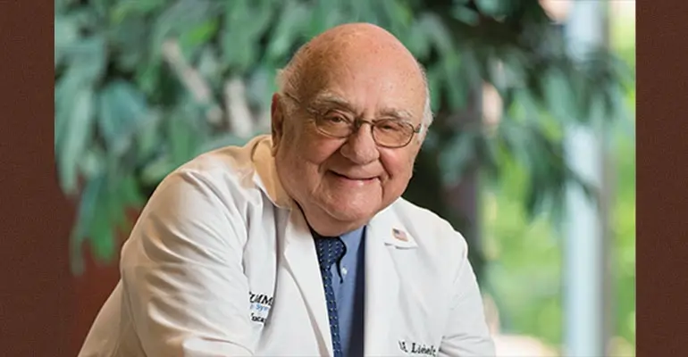 Dr. Robert Liebelt, the first dean of the College of Medicine at NEOMED, in a white coat with greenery in the background.