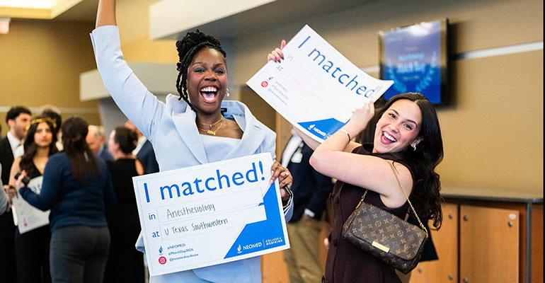 Two students celebrate indoors holding “I matched!” signs, smiling and raising their arms during a Match Day event.