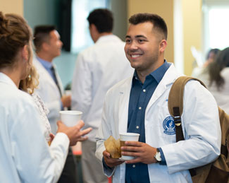 Two medical students talk while holding coffee during a social activity.