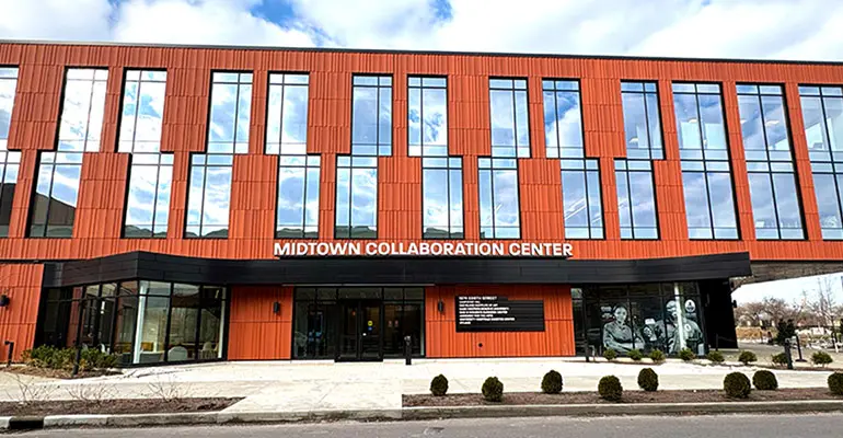 The exterior of the Midtown Collaboration Center, a two-story building with orange metal paneling, large vertical windows, and a black entrance canopy along a city street.