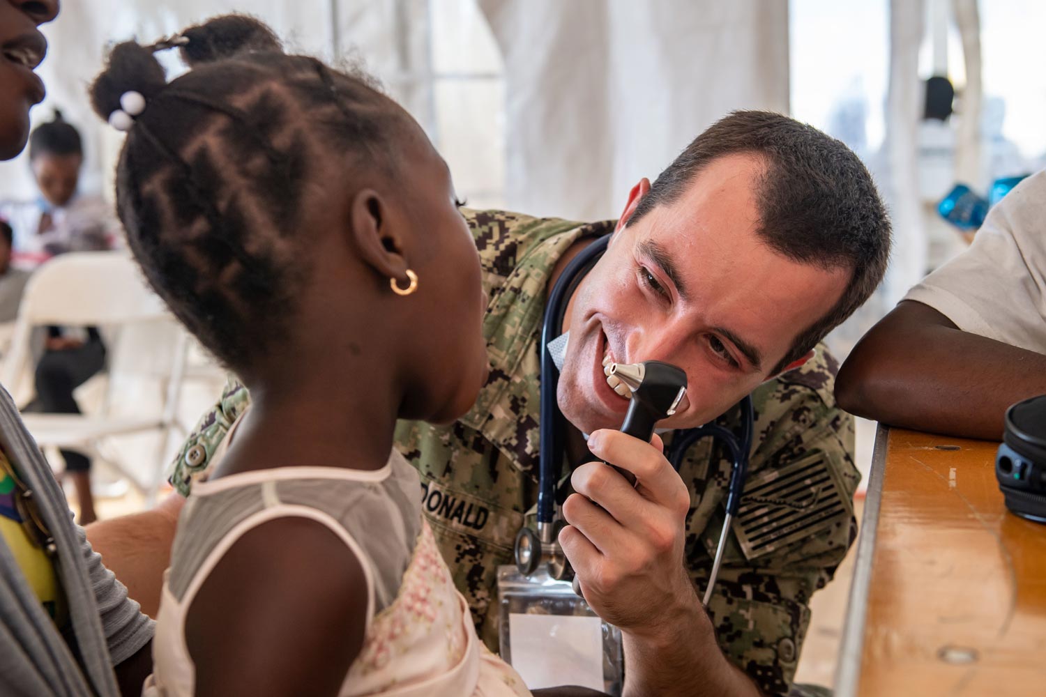 A smiling navy doctor checks a young patient.