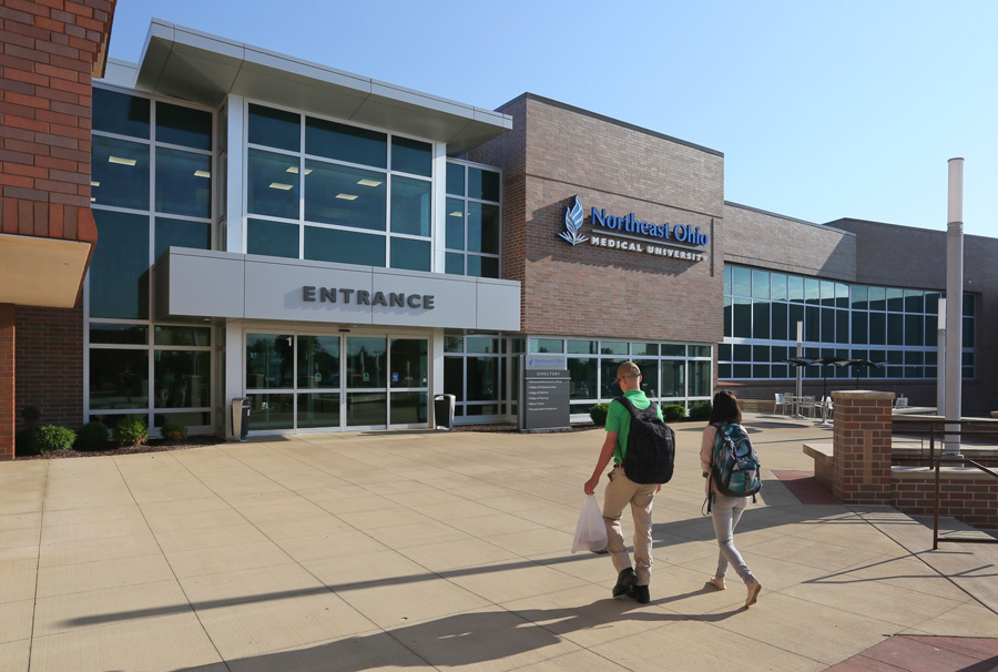 Two students with backpacks walk into NEOMED on a summer morning.