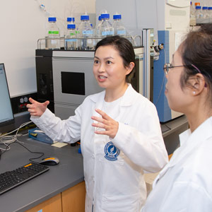 A researcher in a white coat gestures while making a point in a lab.