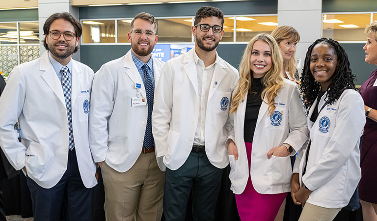 Five NEOMED students in white coats talk at a University event.