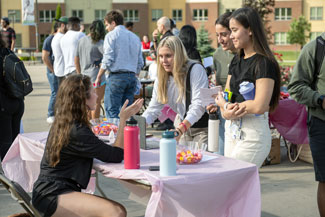 Three medical students talk with a woman at a table during an outdoor fair at NEOMED.
