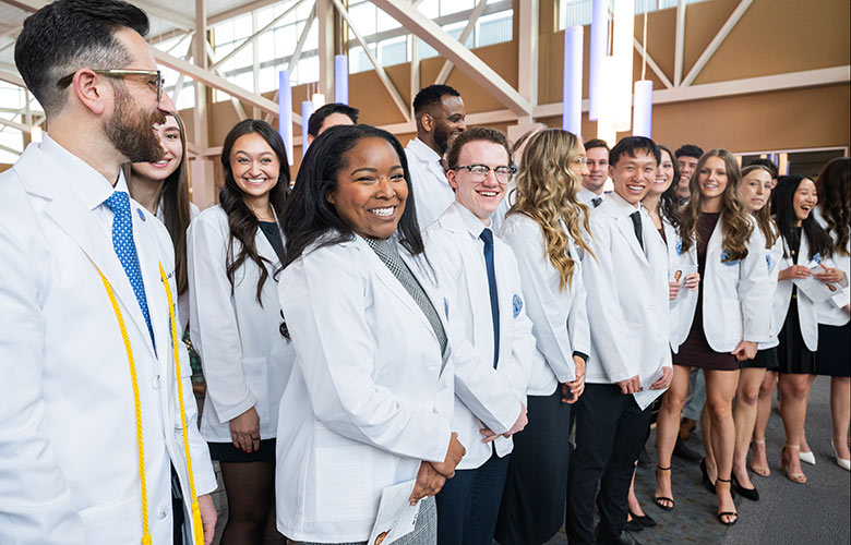 About 20 students stand as a group for a photo, all wearing their white coats for the first time.