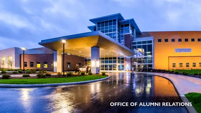 The exterior of NEOMED on a rainy evening, with reflections of the building on the wet pavement.