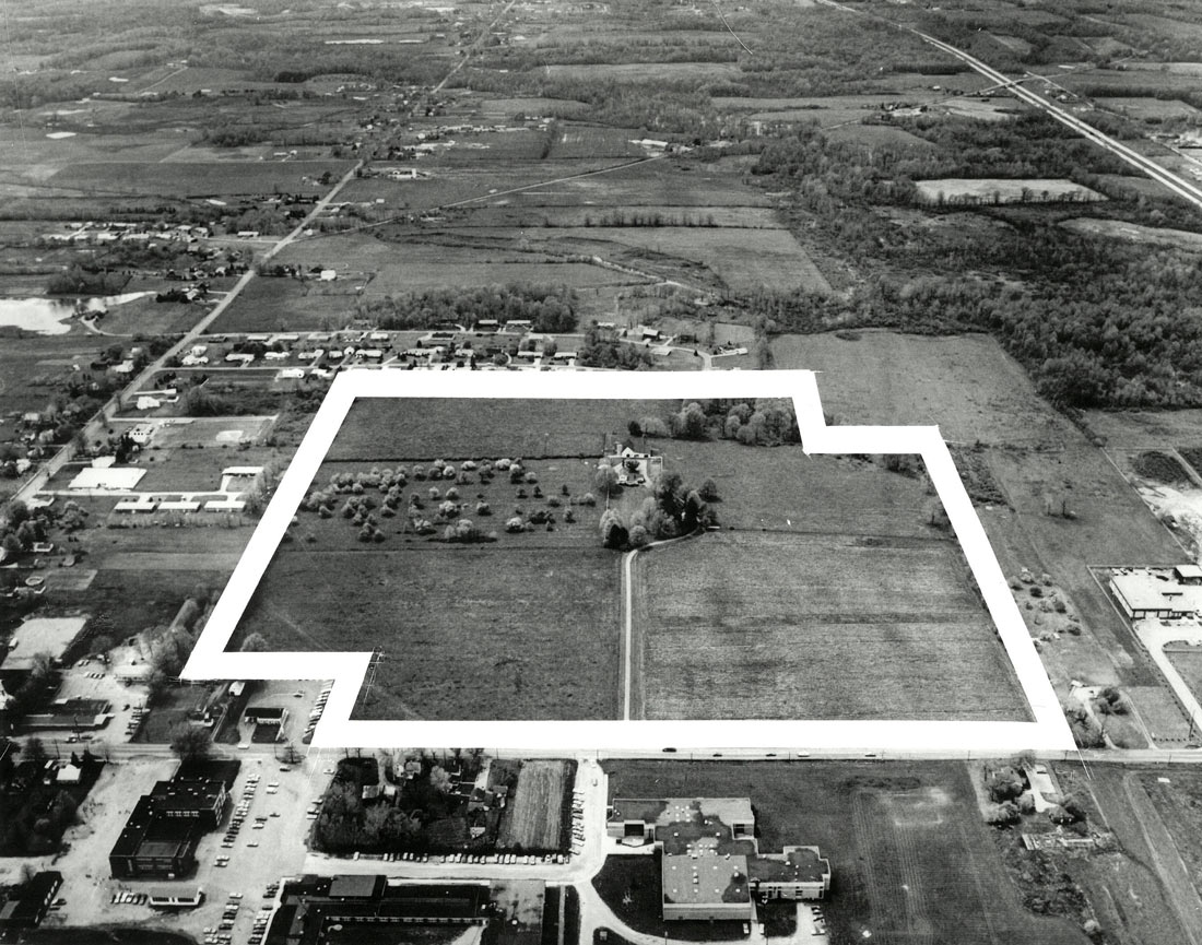An aerial photograph shows farmland outlined in white to indicate the planned building site.