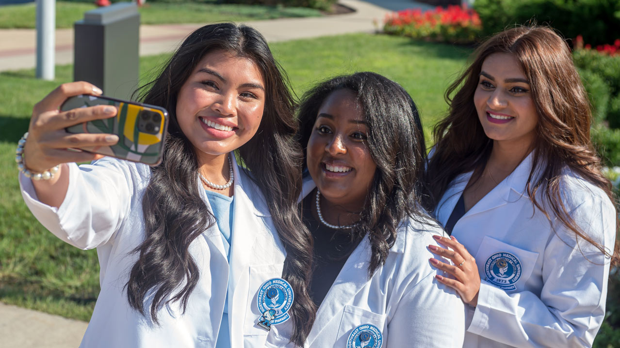 Three pharmacy students in white coats pose for a selfie.