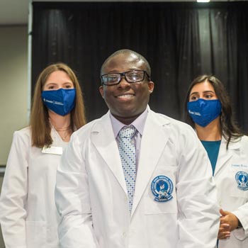A smiling pharmacy student wears his white coat for the first time.