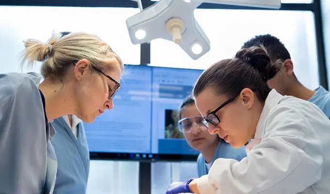 Students and faculty in medical gear look at a patient.