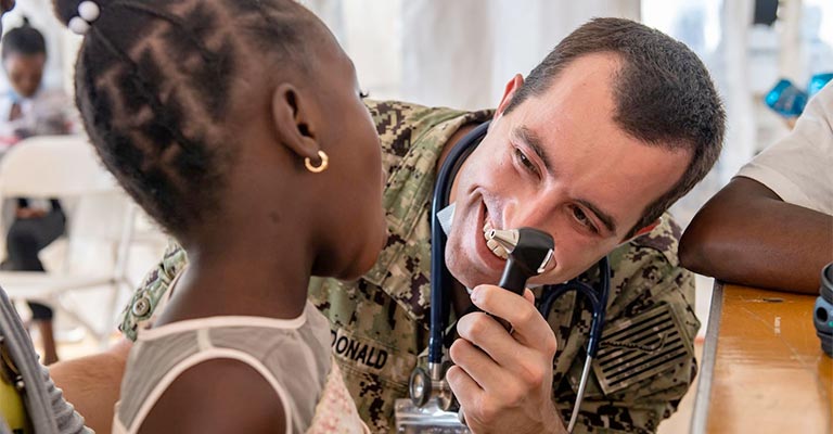A physician in military dress cares for a young patient.