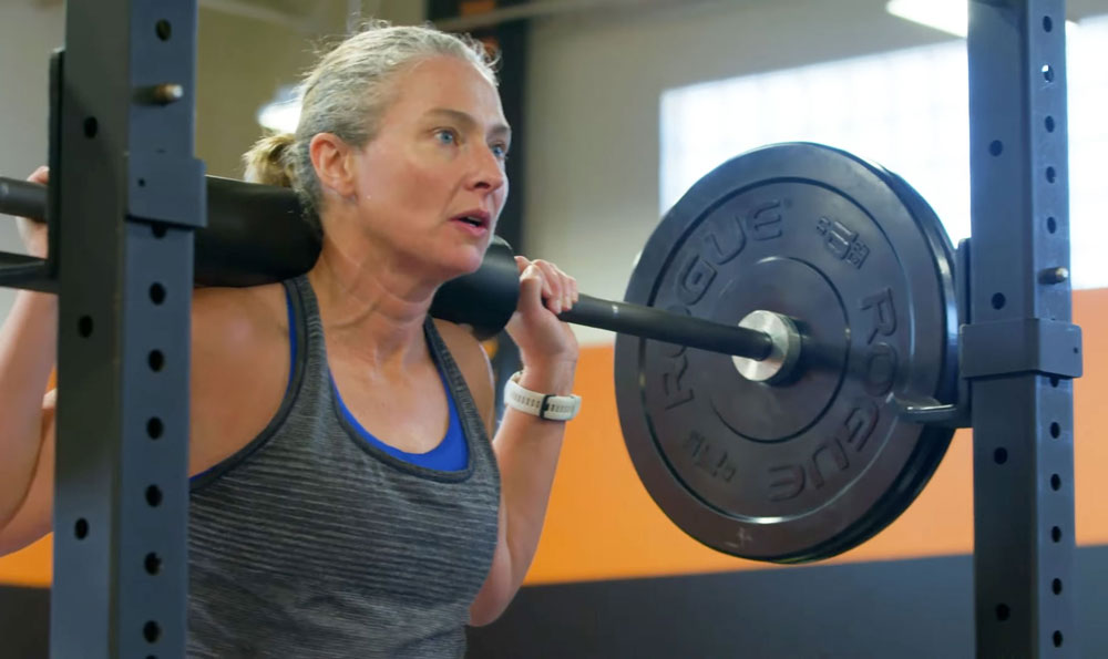 A woman in workout gear focuses while lifting weights.
