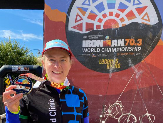 A smiling woman holds her finishers' medal after completing an Ironman event in Utah.