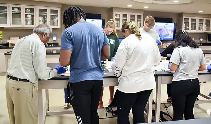 Students at a table observing how to carry out a procedure.