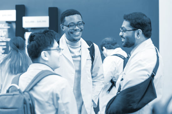 Three medical students talk in a bright hallway while enjoying cups of coffee.