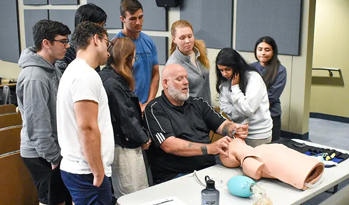 A group of students watch a faculty member demonstrate a procedure.