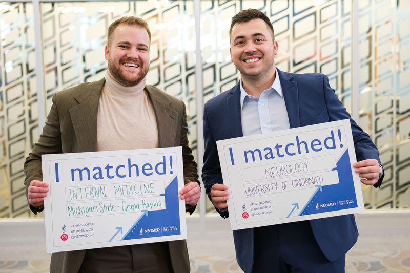 Two fourth-year medical students hold signs showing where they will be going for residency.