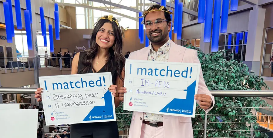 Two NEOMED medical students stand indoors holding signs that read “I matched!” with their residency placements, smiling in a large atrium during a Match Day event.