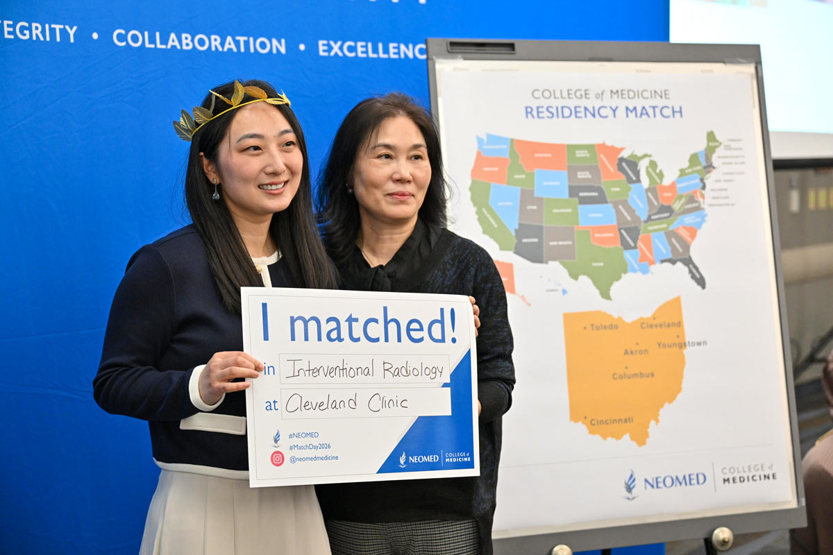 A student stands with a supporter holding an “I matched!” sign for interventional radiology at Cleveland Clinic, with a residency map displayed behind them.