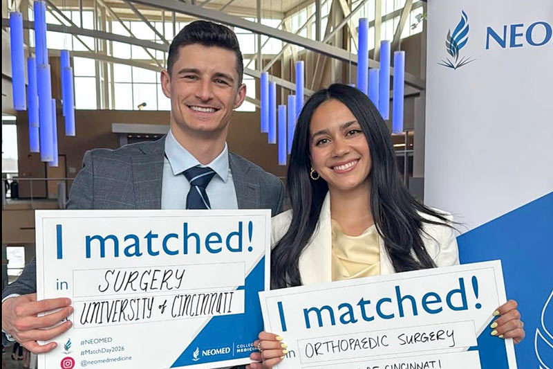 Two fourth-year medical students hold signs showing where they will be going for residency.