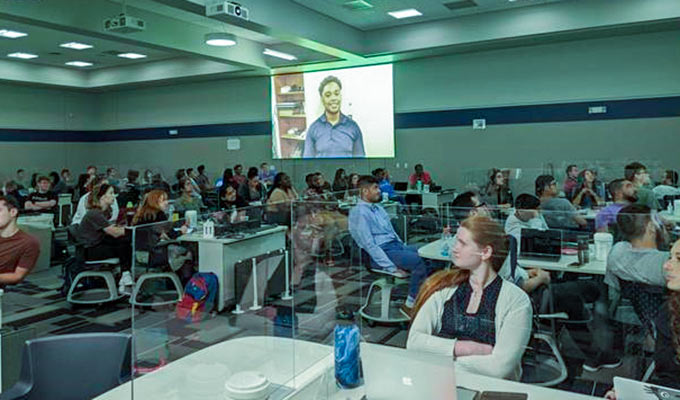 Students watch a presentation on a large screen in a large conference hall.