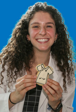 A medical student smiles while holding a cutout cookie of a physician's white coat.