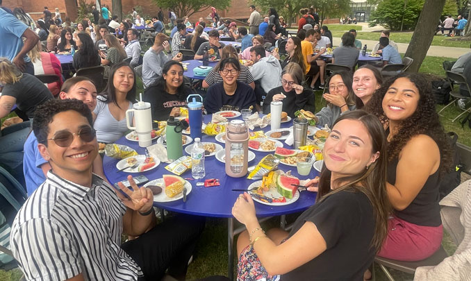 Student crowded around a table during a campus picnic in the university courtyard
