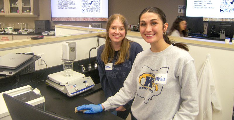 Two members of the pharmacy club hold pharmacy tools in a NEOMED lab.