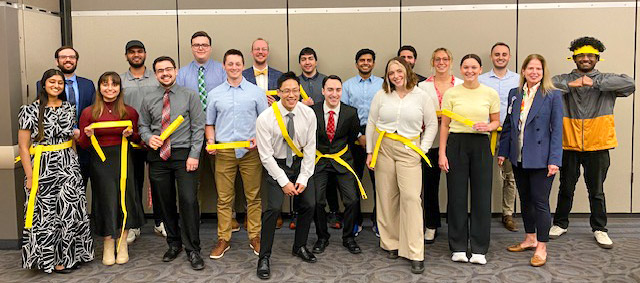 A group of Health Systems Science students stand as a group holding yellow belts.