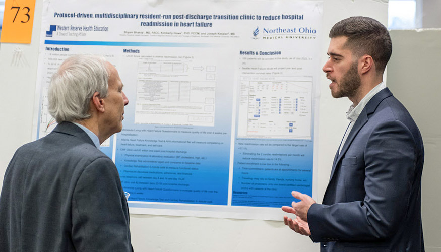 A student in a coat and tie discusses his research project with a dean during a NEOMED symposium.