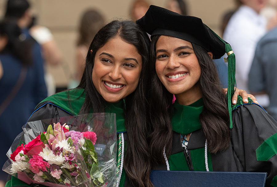 Two graduates hold flowers as they pose for a photogragh.
