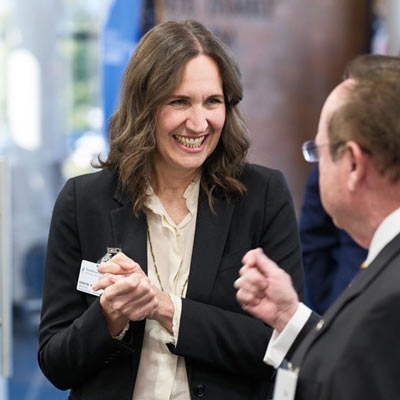 A women laughs while chatting with a colleague at an indoor campus event.