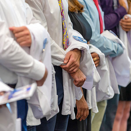 The arms and hands of new medical students, where you can see the sleeves of the white coats they are wearing for the first time.