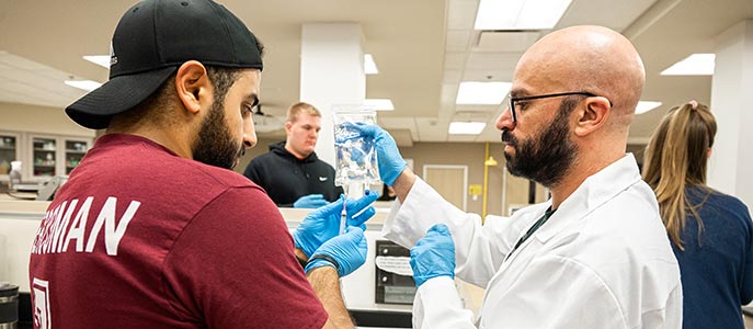A faculty member works with a student in a pharmacy lab.