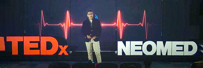 A physician speaks from a dark stage, with the word TEDxNEOMED behind him.