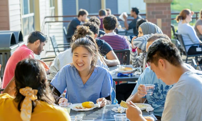 NEOMED students laugh as they enjoy food at outdoor tables during a break.