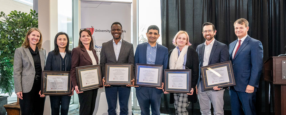 A group of faculty in business dress hold certificates honoring their appointment as faculty scholars.