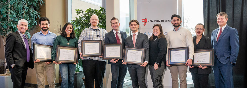 A group of student researchers in business dress hold certificates honoring their appointment as student scholars.