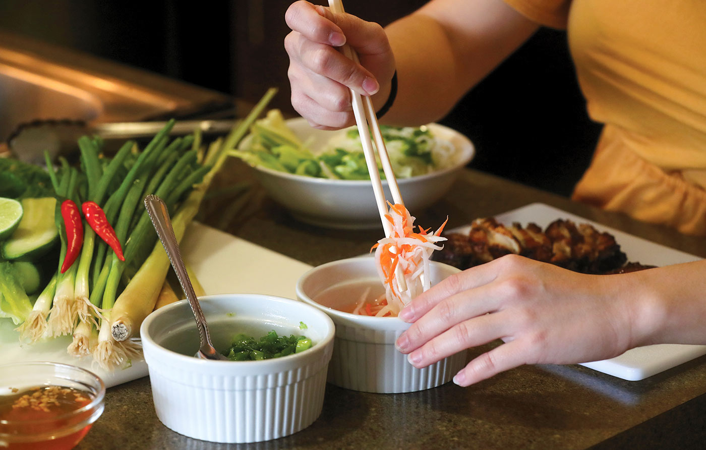 Hands preparing a chicken vermicelli bowl.